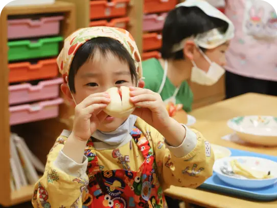エプロンと三角巾を身につけ、手作りのいちごサンド（フルーツサンド）を嬉しそうに食べる男の子