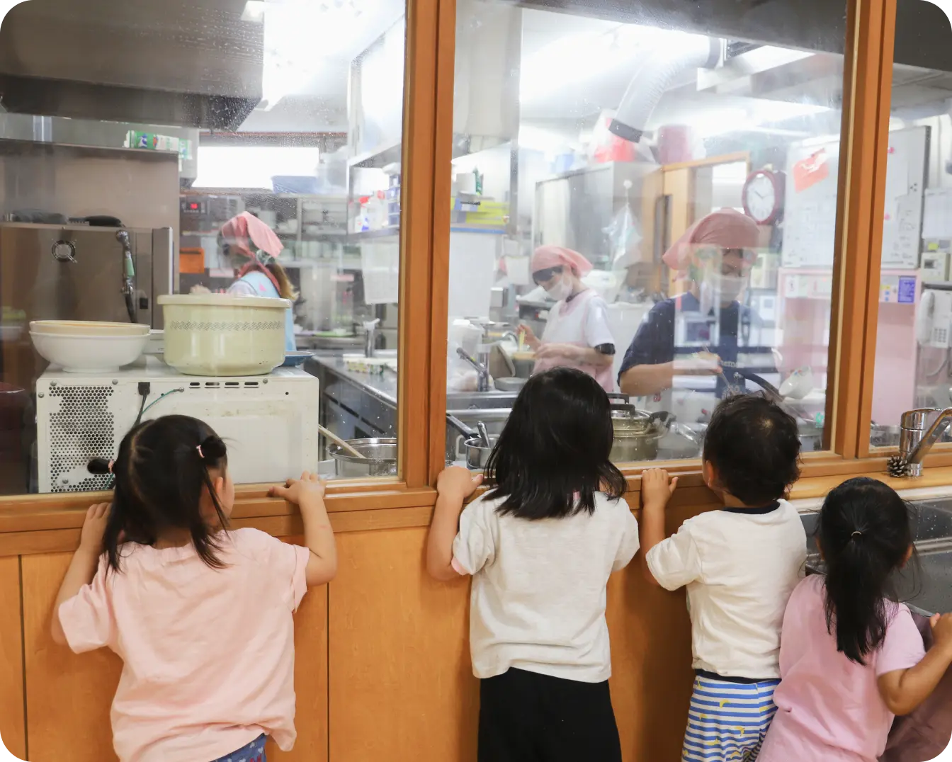ガラス張りの調理室の外から、調理スタッフが給食を作っている様子を興味津々で覗き込むつくしんぼ保育園の園児たち