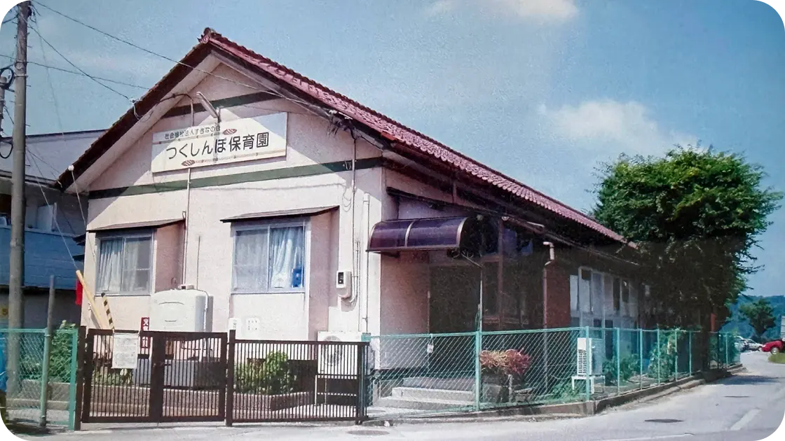 「つくしんぼ保育園」の看板が掲げられた、三角屋根と緑色のフェンスがある平屋の園舎外観