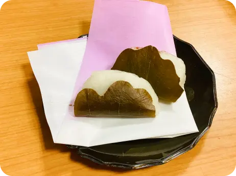 黒い皿に敷かれた敷き紙の上に並べられた、2つの柏餅の様子
