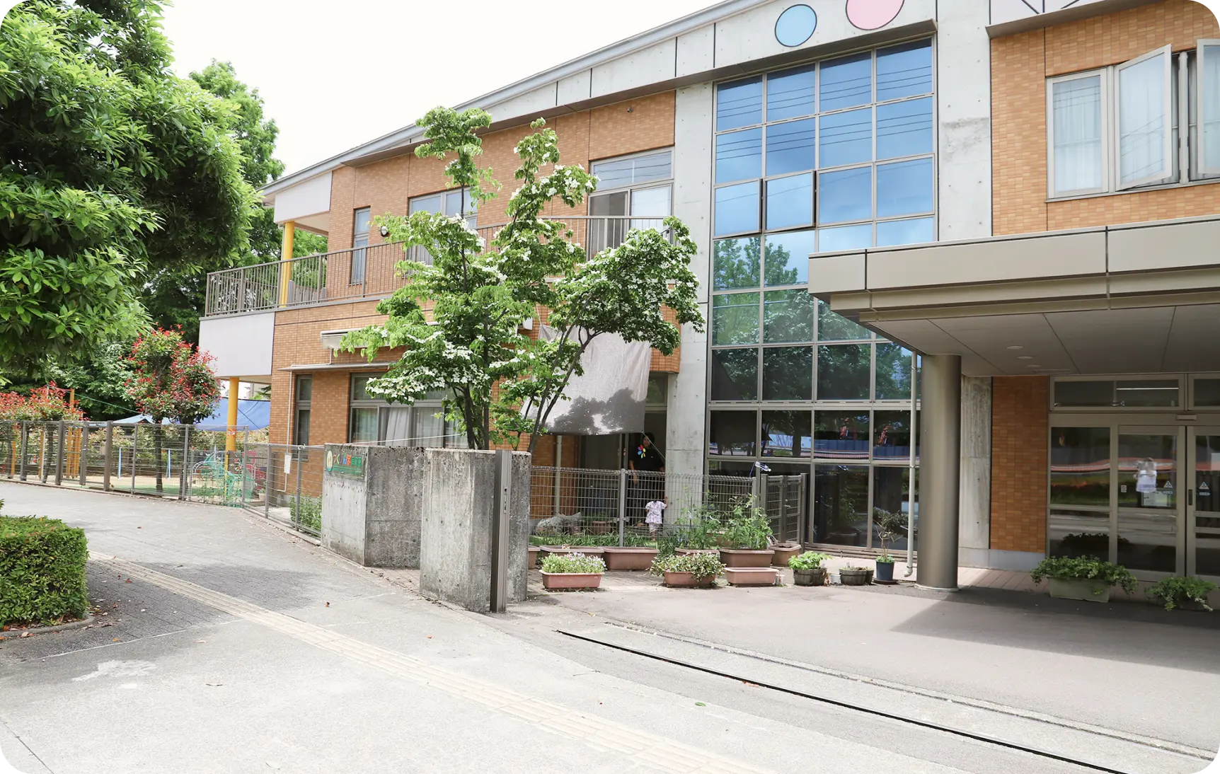 大きなガラス窓と茶色のレンガ調の外壁が特徴的な、2階建ての現代的な保育園舎の外観写真