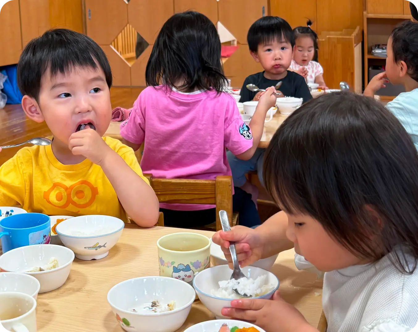 保育室のテーブルを囲み、それぞれ自分でスプーンを持って一生懸命に給食を食べる子どもたちの様子