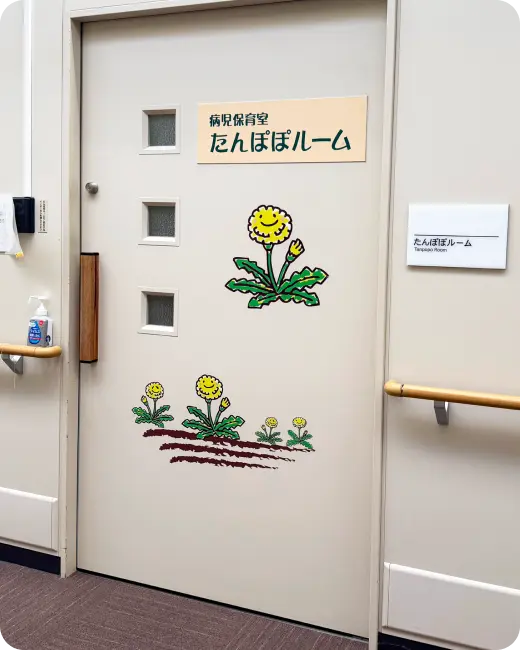 「病児保育室 たんぽぽルーム」の看板と、笑顔のたんぽぽのイラストが描かれた部屋の入り口のドア