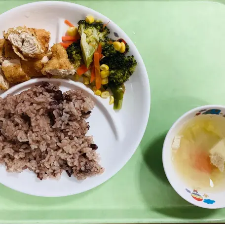 ワンプレートに盛られたお赤飯、カツ、ブロッコリーのソテーと、汁物がセットになった給食の様子